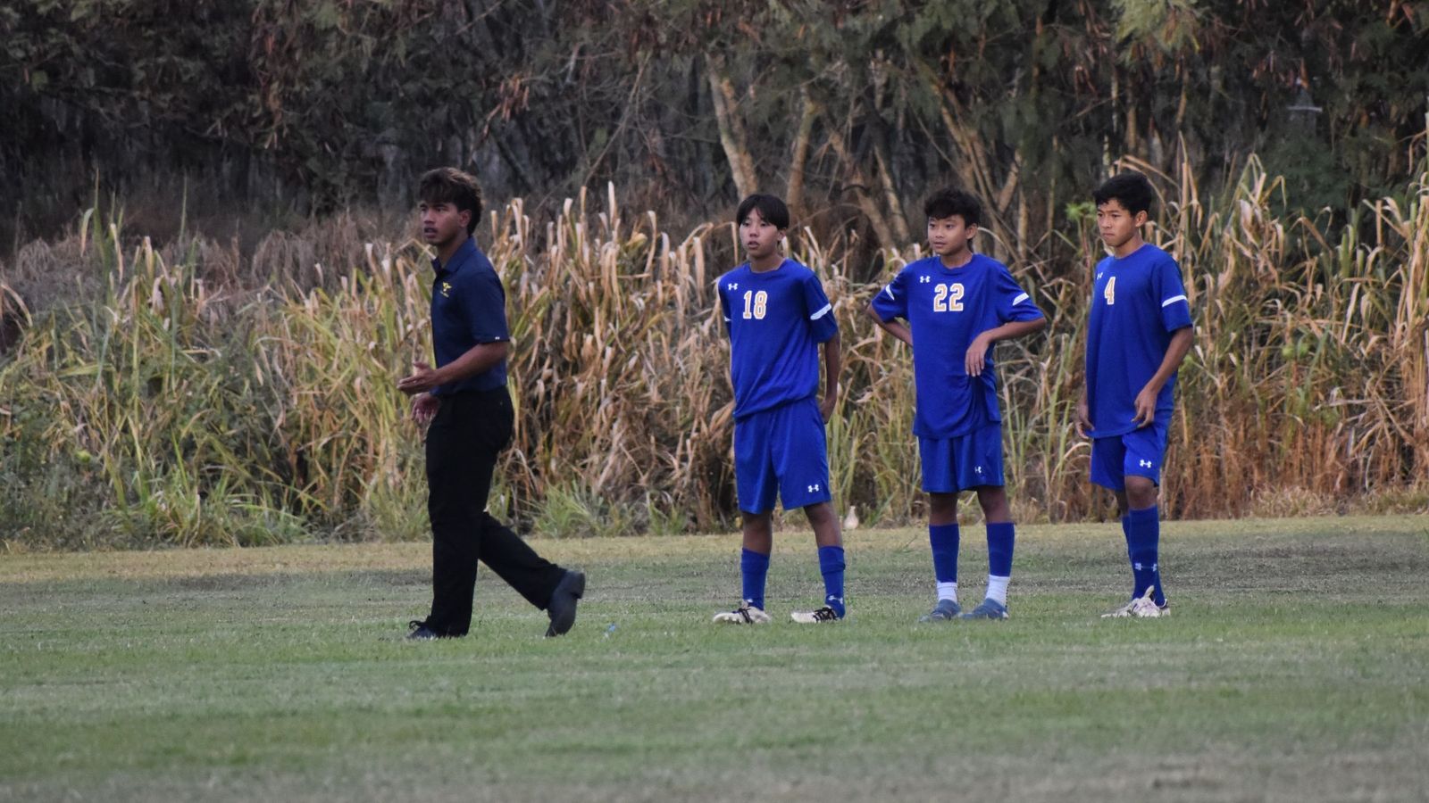 Coach Joe on a grass field with three youth players in blue uniforms