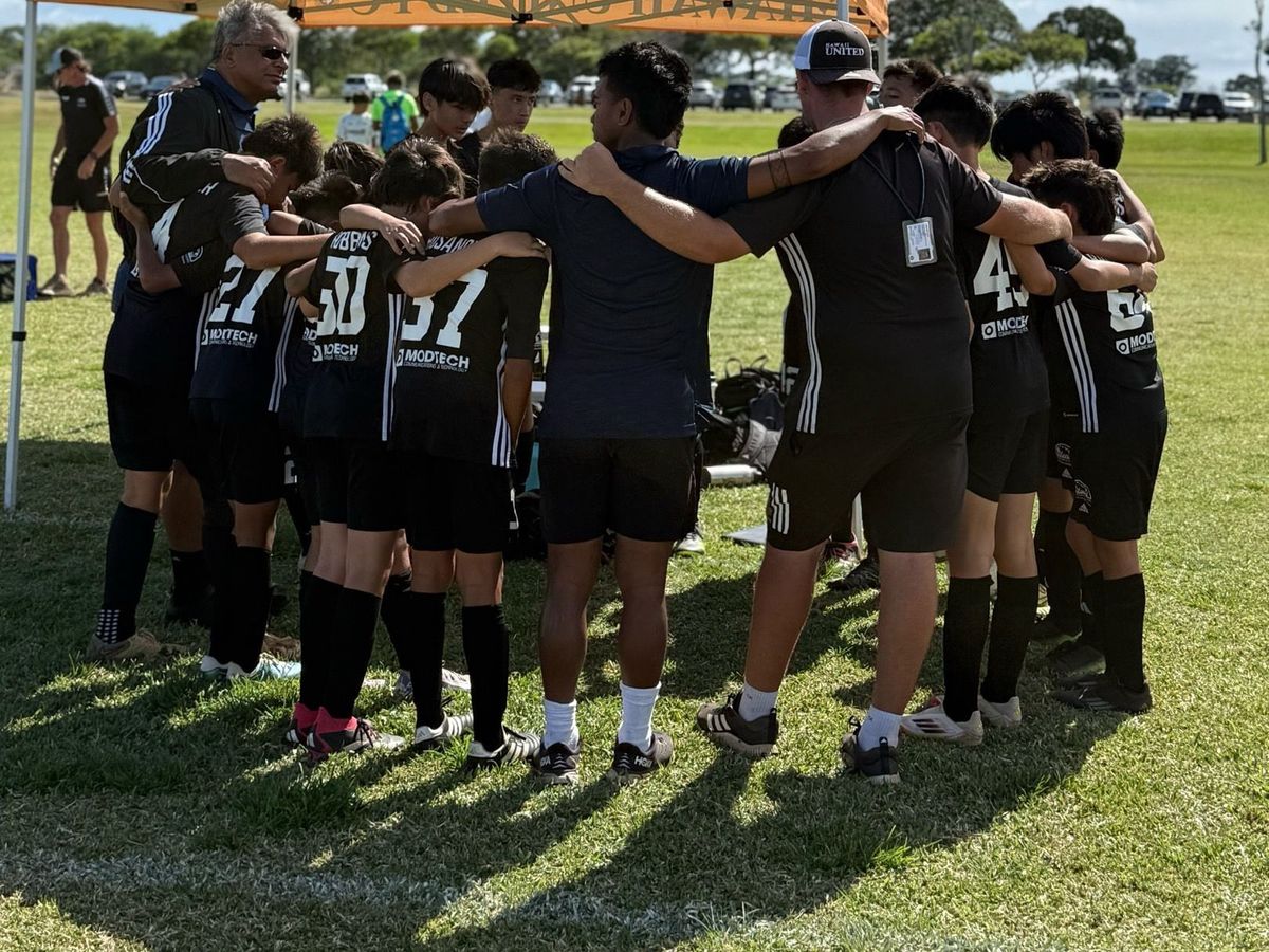 A youth soccer team and coaches in a huddle on a sunny field